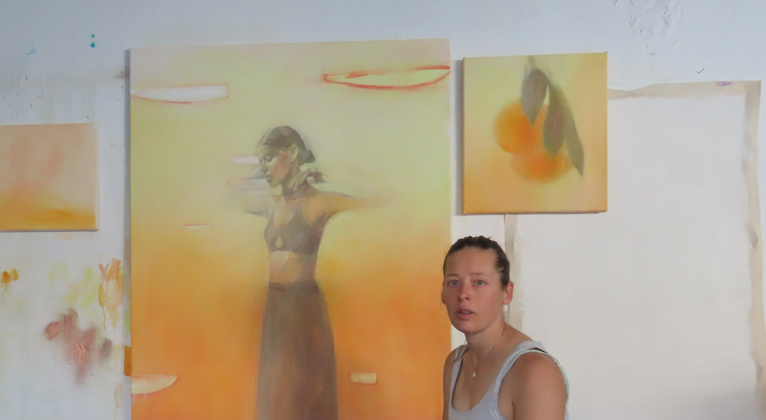 In the artists studio orange paintings on the wall with the artist in front