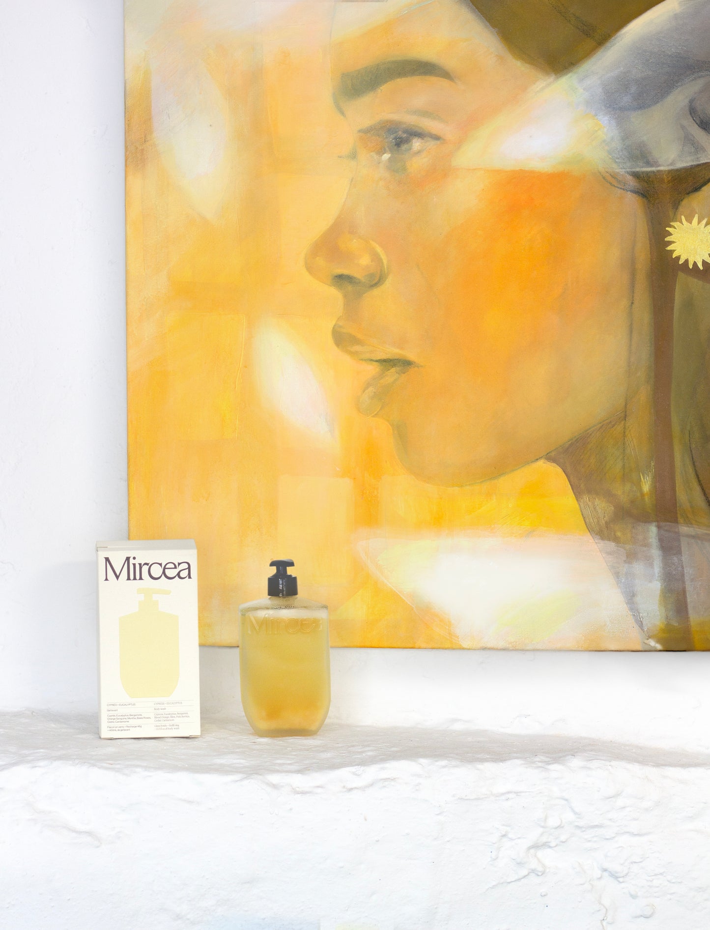 Orange portrait painting hanging on a white wall with Mircea Care products below.