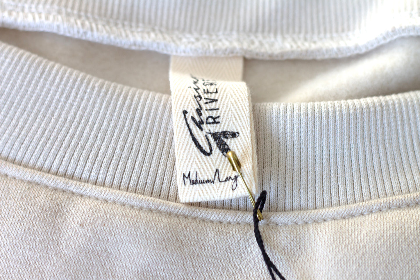 Close-up of the Chasing Rivers clothing label on the Grounded sweatshirt from the Studio Hannah Chloe collaboration, made from organic cotton.