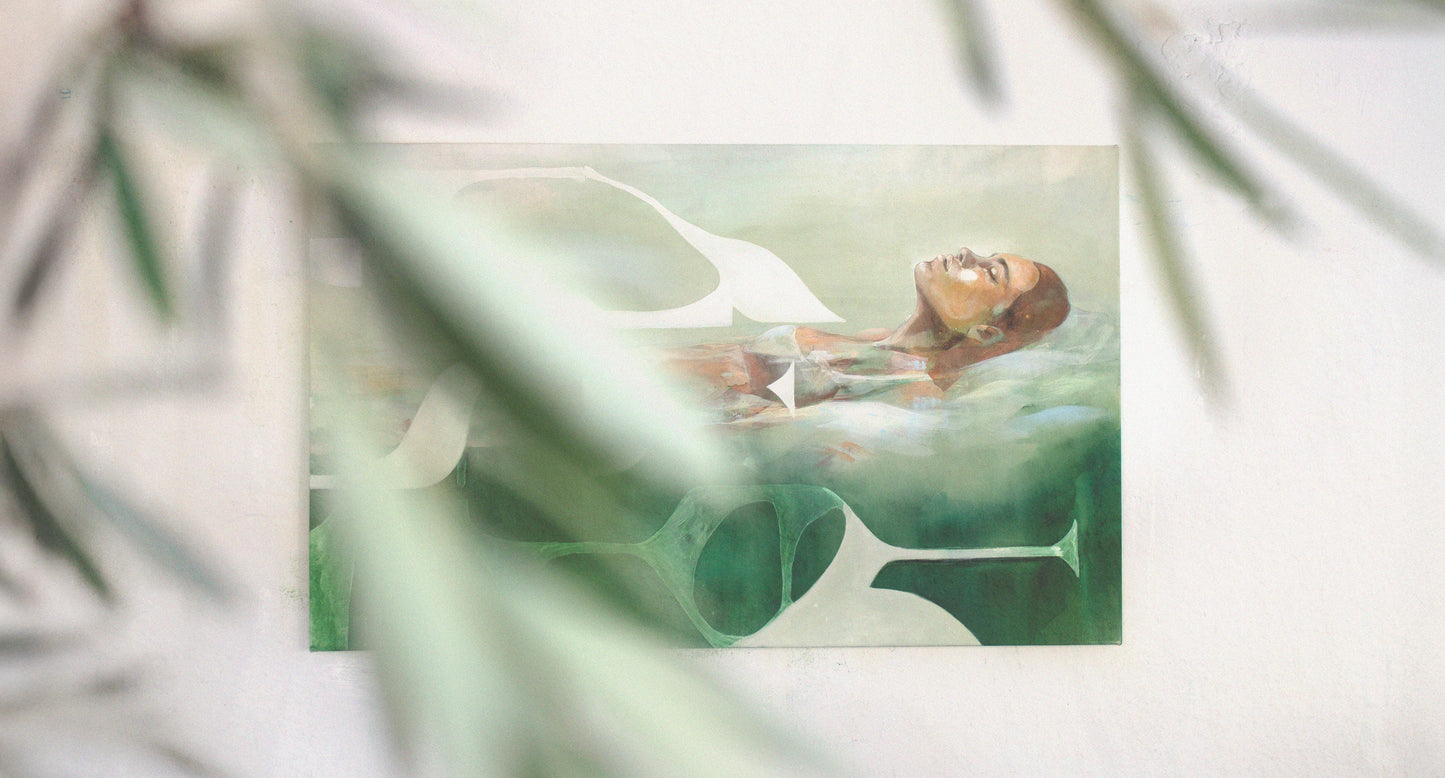 Photograph of a contemporary acrylic painting titled Mediterranean Musing by Hannah Adamaszek, featuring a serene woman floating in water, surrounded by abstract organic shapes in soft green and earthy tones. The painting is displayed on a white wall, partially obscured by blurred green foliage in the foreground, adding depth and a natural ambiance.