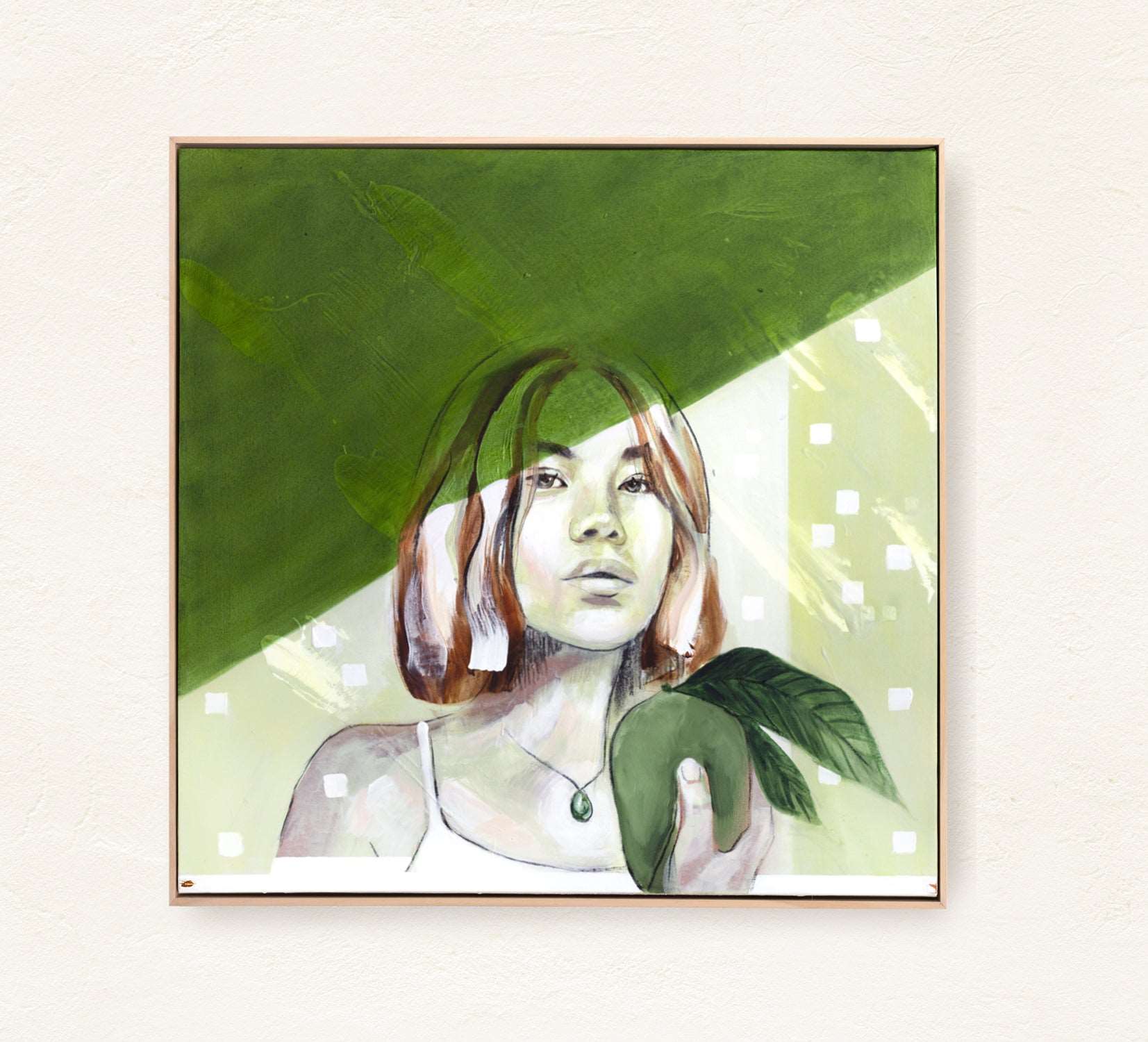 A contemporary abstract portrait of a woman holding a green fruit with leaves, painted in earthy green and warm tones. Framed in a natural wood on a mediterranean style plaster wall.