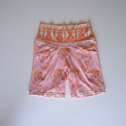 Flatlay of the Calypso bike shorts by Chasing Rivers featuring Hannah Chloe’s pink and peach mermaid artwork with a high-rise seahorse waistband.