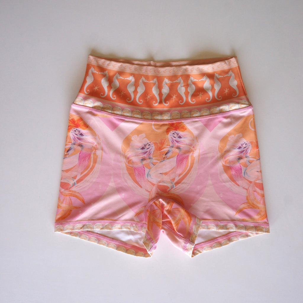 Calypso high-waist shorts by Chasing Rivers featuring Hannah Chloe’s mermaid and seahorse artwork in soft pink and peach tones, laid flat on white background.