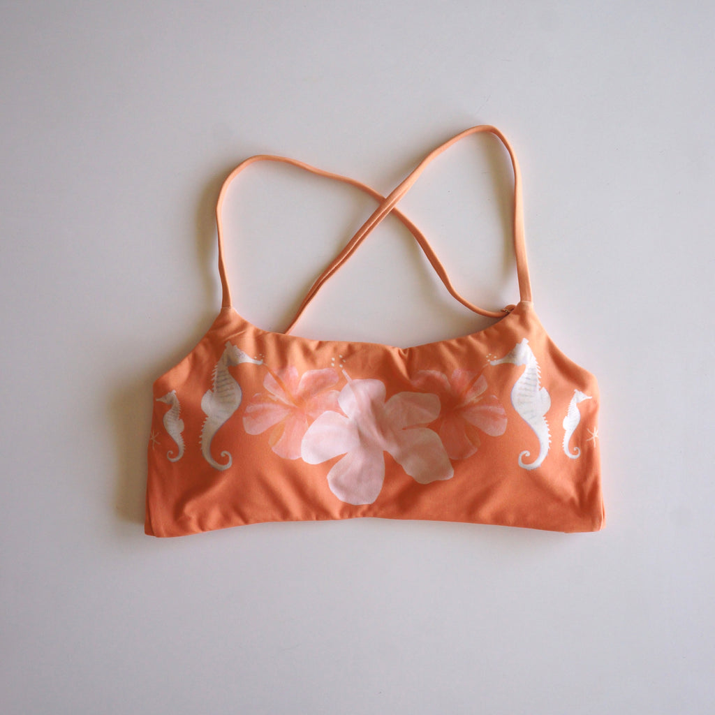 Flatlay of the Chasing Rivers x Hannah Chloe Calypso orange floral crop top featuring white seahorse details and soft hibiscus artwork on a white background.