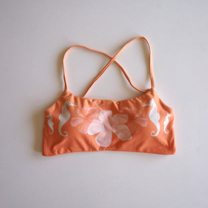 Flatlay of the Chasing Rivers x Hannah Chloe Calypso orange floral crop top featuring white seahorse details and soft hibiscus artwork on a white background.