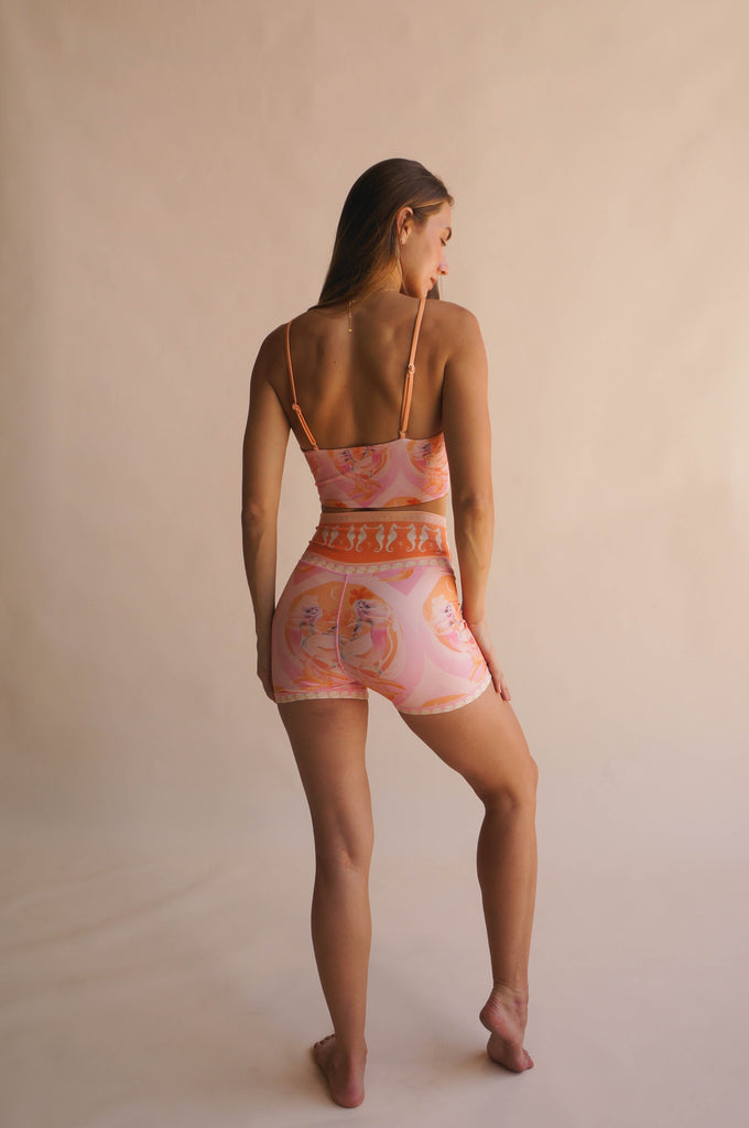 Back view of model wearing the Chasing Rivers x Hannah Chloe Calypso pink illustrated crop top and matching high-waisted shorts, standing against a warm neutral backdrop.
