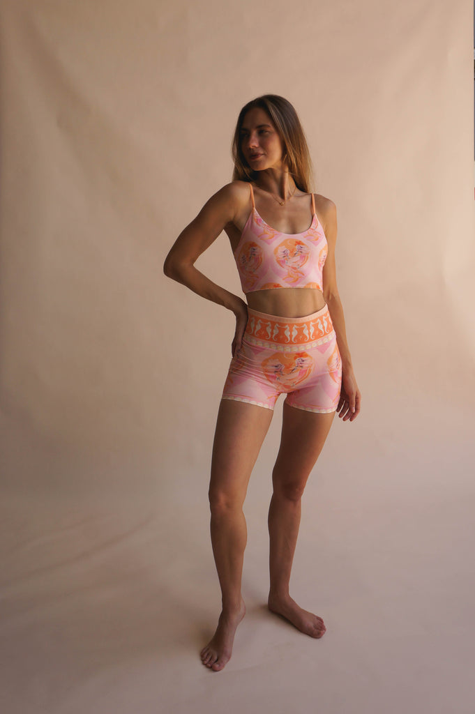 Full-body shot of model wearing the Chasing Rivers x Hannah Chloe Calypso pink illustrated crop top and matching high-waisted shorts, standing against a warm neutral backdrop.