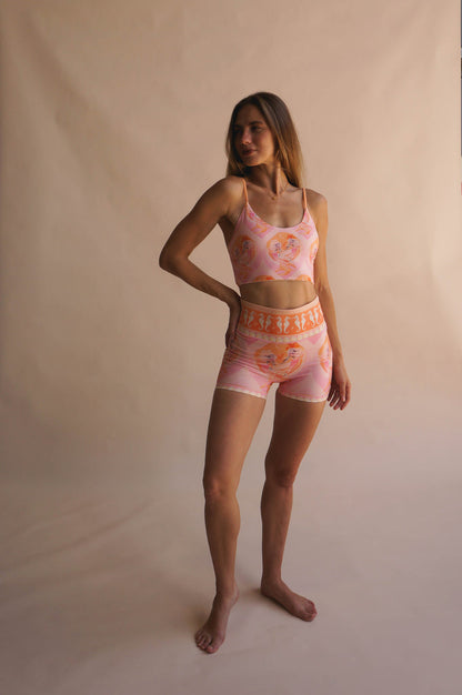 Full-body shot of model wearing the Chasing Rivers x Hannah Chloe Calypso pink illustrated crop top and matching high-waisted shorts, standing against a warm neutral backdrop.