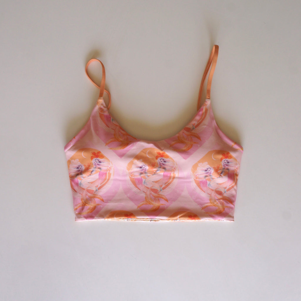 Flatlay of the Chasing Rivers x Hannah Chloe Calypso pink illustrated crop top featuring soft peach and pink feminine artwork on a white background.