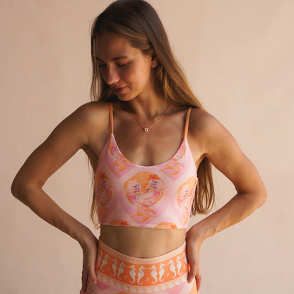 Model wearing the Chasing Rivers x Hannah Chloe Calypso pink illustrated crop top with soft peach and pink artwork, standing against a warm neutral backdrop.