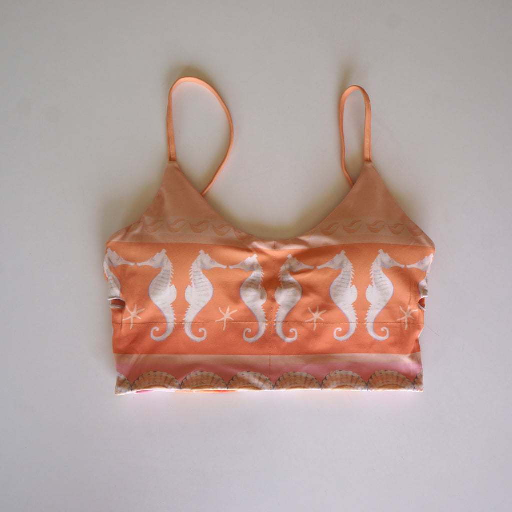 Flatlay of the Chasing Rivers x Hannah Chloe Calypso crop top featuring a peach and white seahorse print with coastal-inspired details on a white background.
