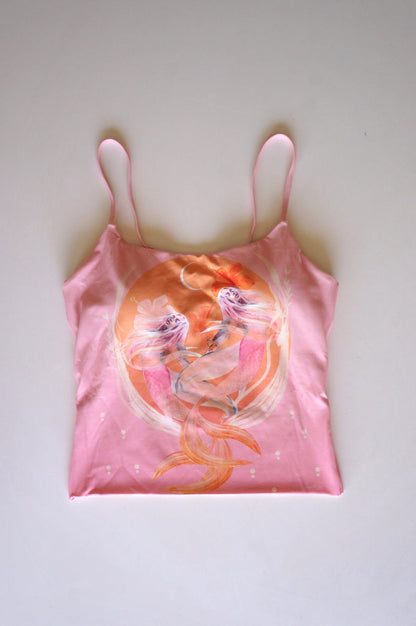 Flatlay of the Chasing Rivers x Hannah Chloe pink illustrated cami featuring soft peach and pink feminine artwork with flowing figures on a white background.