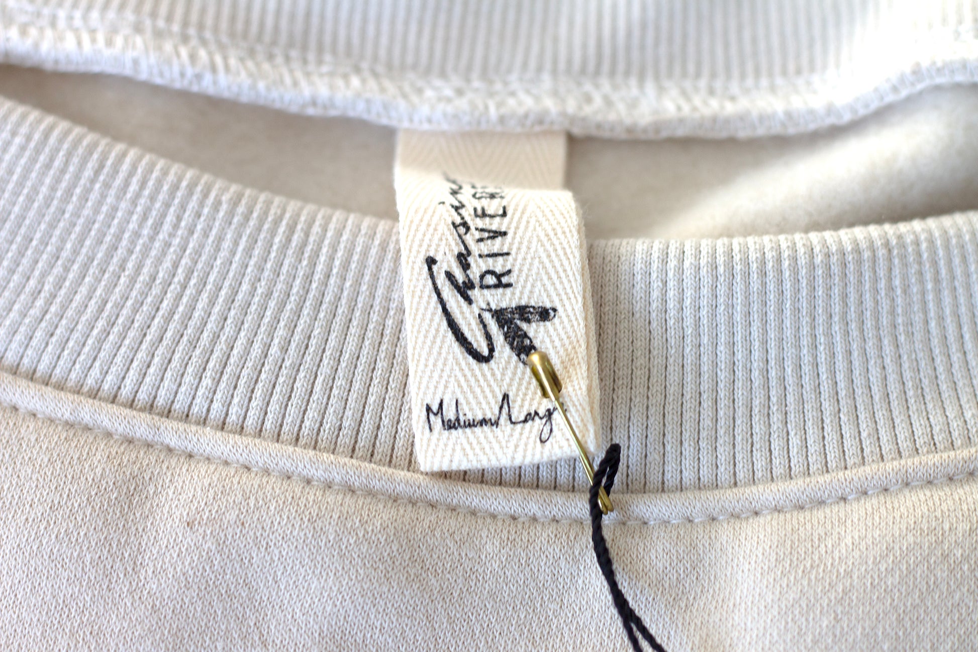 Close-up of the Chasing Rivers clothing label on the Grounded sweatshirt from the Studio Hannah Chloe collaboration, made from organic cotton.
